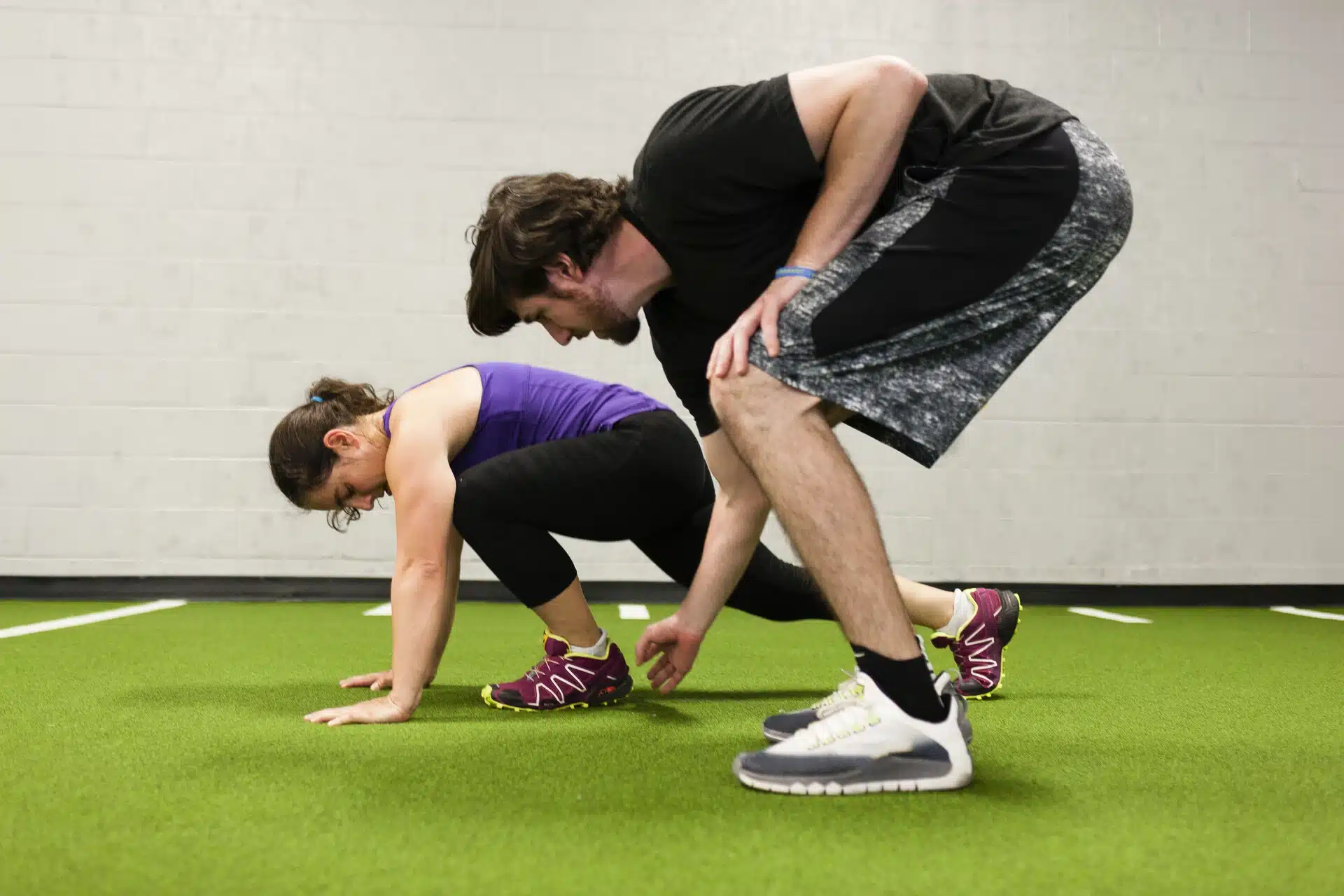 Sports Physiotherapy Edmonton 5 Trainer assisting a woman with a low crawl exercise during a Sports Physiotherapy Edmonton session on indoor turf.