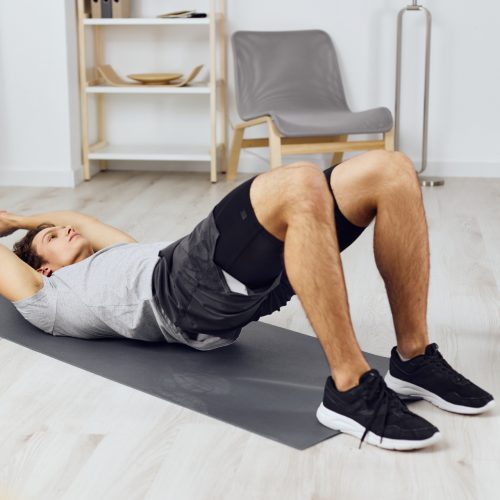 Man performing a glute bridge exercise with dumbbells on a yoga mat at home, demonstrating Pelvic Floor Physiotherapy Edmonton techniques.